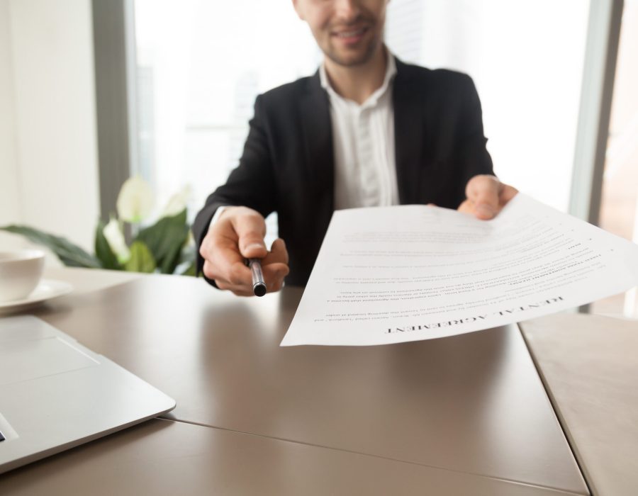 Real estate agent offers to sign rental agreement Realtor reaching out pen and rental agreement to clients. Real estate consultant sitting at desk in office and offers to read and sign contract document. Readiness to make a deal, rent new dwelling