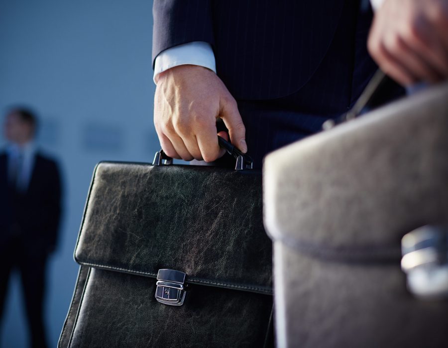 Business partners Cropped image of business partners carrying briefcases on the foreground while their colleague standing on the background